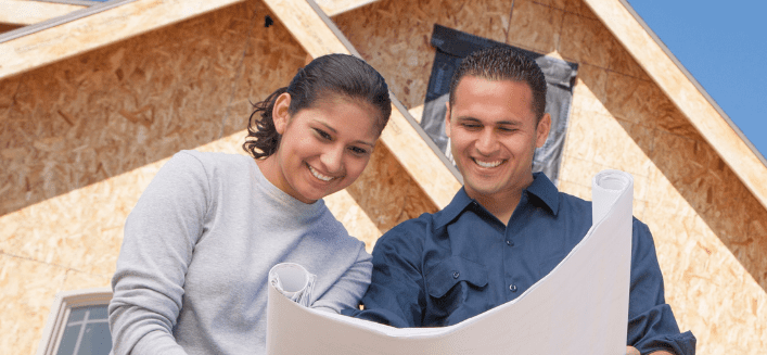 A man and woman looking at a blueprint in front of an unfinished house to build a dream home.