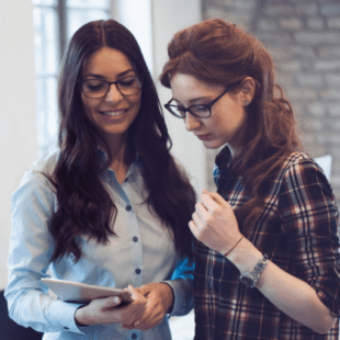 An image of two women reading off a tablet.