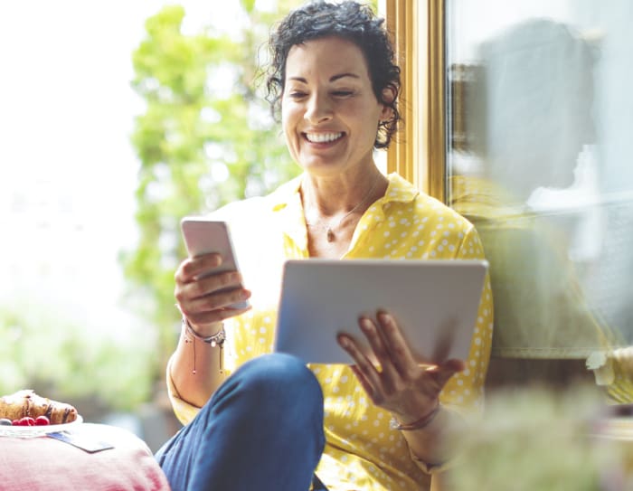 A woman sitting down looking at her phone and holding a tablet.