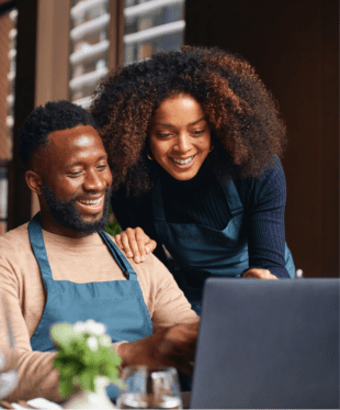 An image of a man and woman wearing aprons looking at a laptop screen.